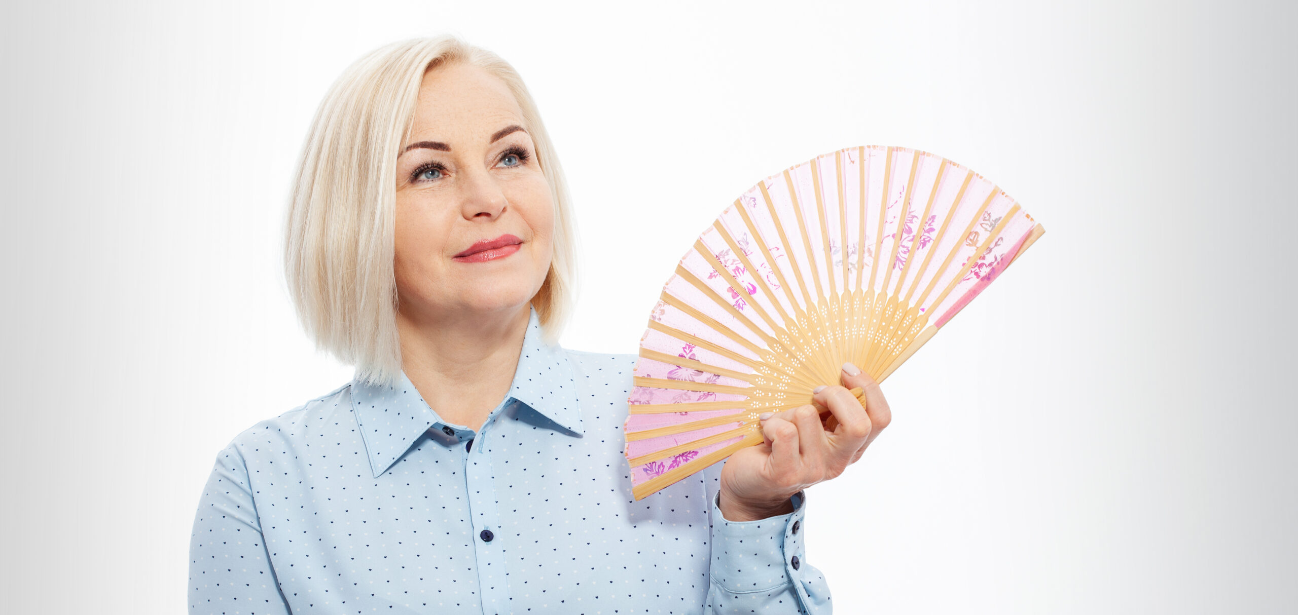 Beautiful middle aged woman with menopause blowing by fan. Hormone replacement therapy and mature woman healthcare. Mid age happy women lifestyle. Senior woman isolated on grey background